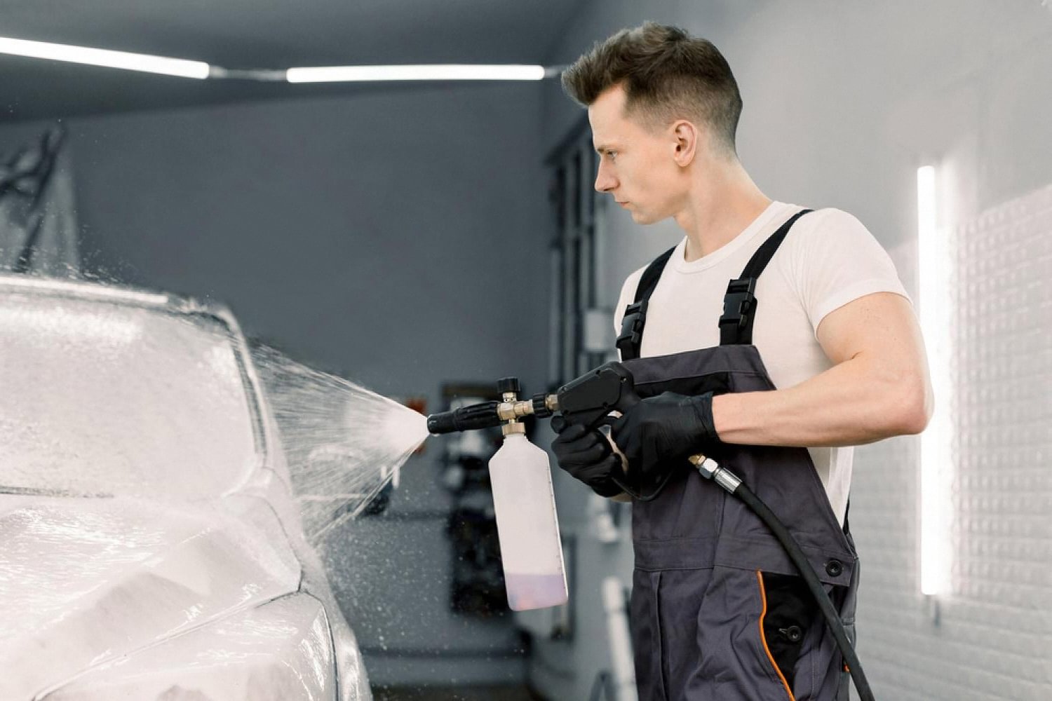 Detailer applying foam pre-wash to a car in a Dubai studio before protection work