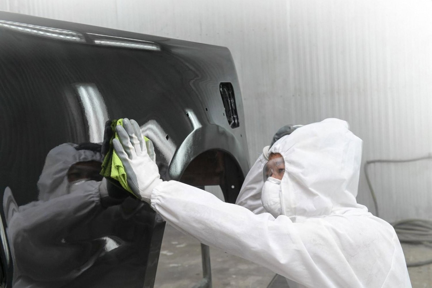 Painter in a full suit inspecting a freshly coated black panel for paint correction