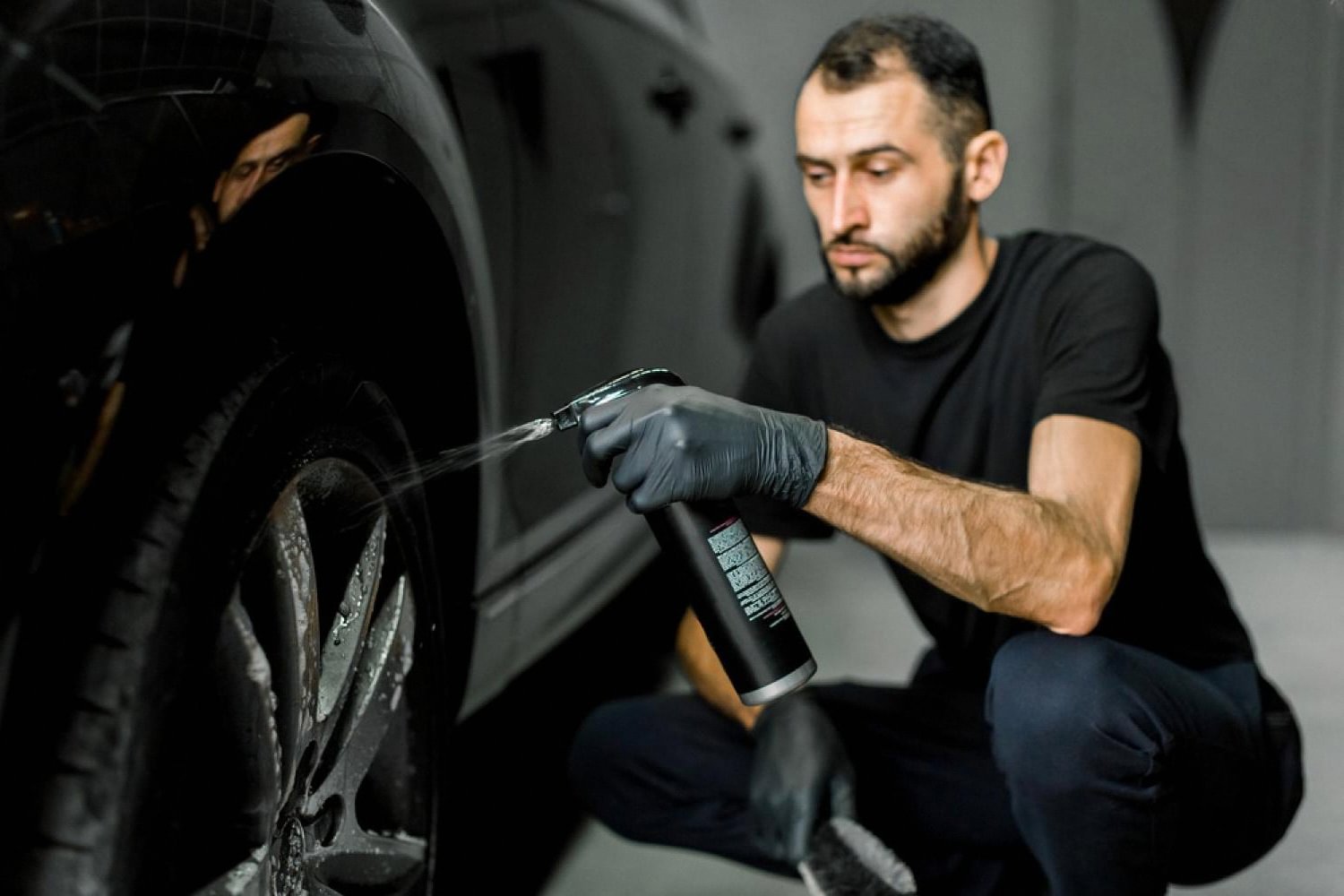 Detailer spraying wheel and tyre protectant on a black SUV