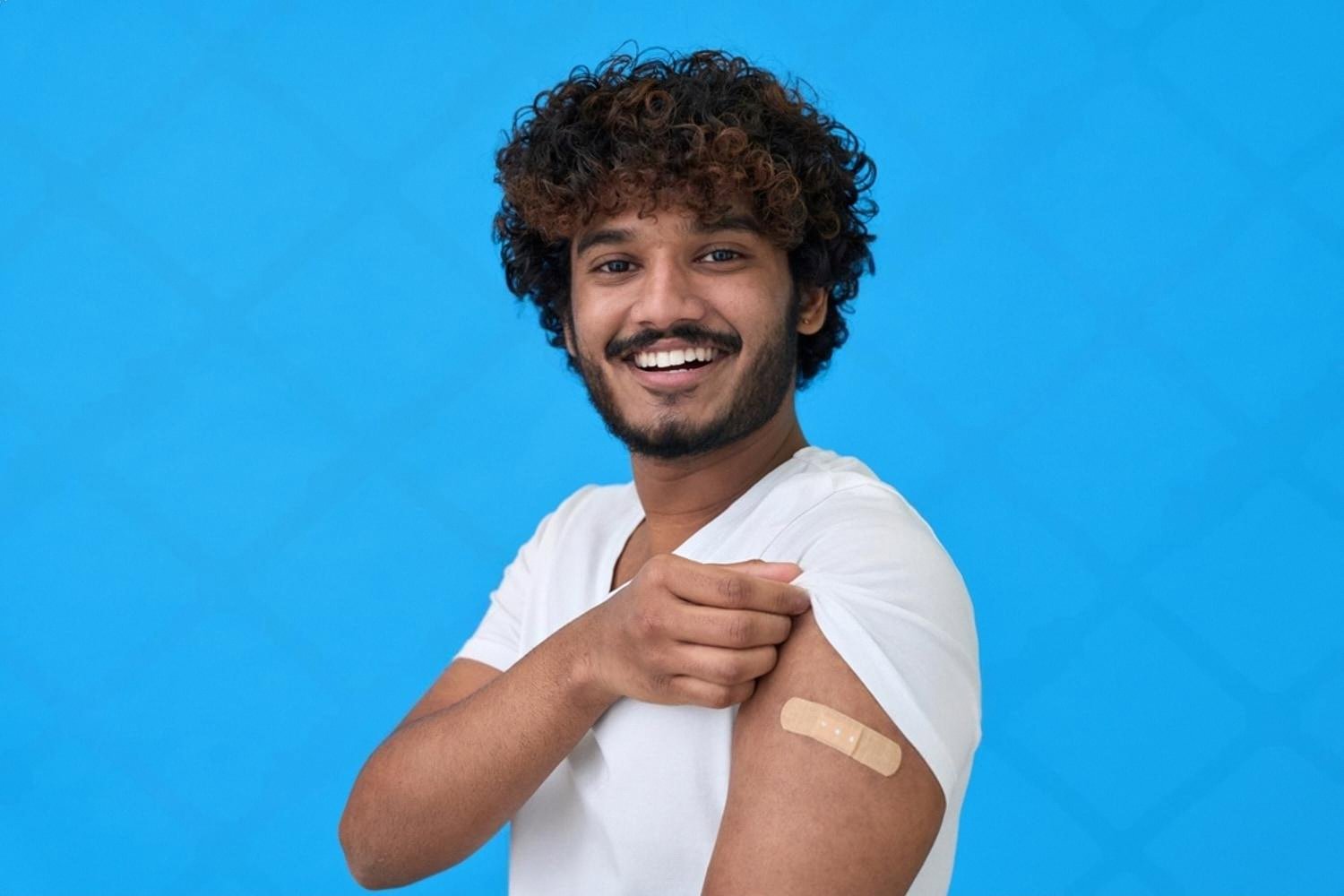 Smiling young man showing a plaster after a vaccination covered by UAE health insurance